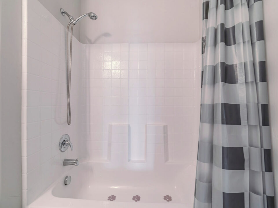 Bathtub with shower and open curtains in a white bathroom